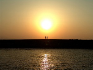 photo of two people walking along the shore backlit by the sun